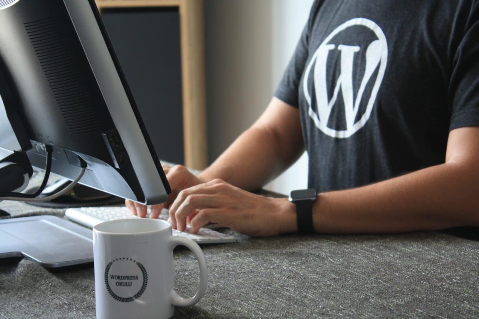 Person typing on a computer wearing a black shirt with the WordPress logo
